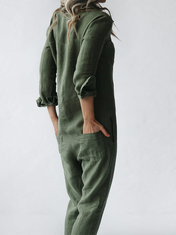 Stijlvolle groene katoenen jumpsuit met lange mouwen, zichtbaar van de zijkant. De persoon heeft een hand in de zak, wat het comfort en de functionaliteit benadrukt. De casual maar elegante uitstraling toont de veelzijdigheid van het kledingstuk.