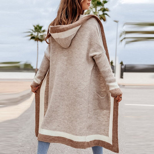 Lange beige cardigan met kapuze gedragen door vrouw op zonnige locatie met palmbomen. Comfortabele en stijlvolle uitstraling, perfect voor casual en chique gelegenheden. Veelzijdig kledingstuk dat warmte en mode combineert.